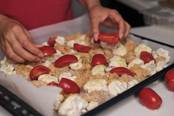 Hands meticulously arranging tomatoes and cauliflower on a tray lined with parchment paper, ready for roasting. This scene reflects the care and effort put into creating balanced and nutritious dishes