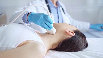 Naklejka premium Doctor man wearing blue medical gloves is using ultrasound equipment on neck of female patient lying down for a medical examination