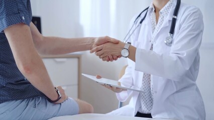 Doctor is shaking hands with a patient while holding a digital tablet in the other hand. Medicine concept