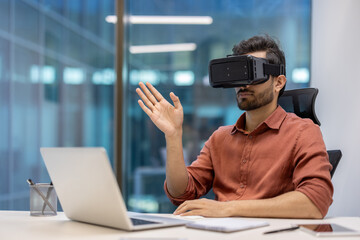 Young professional in modern office using virtual reality headset while interacting with laptop for...