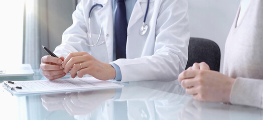 Doctor consulting patient. Male physician is gesturing with his hands over a glass desk while talking with a woman in a clinic, close up. Medicine concept