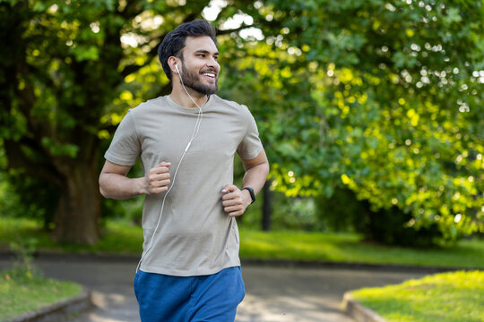 Smiling man jogging in the park with earphones enjoying morning exercise in nature.