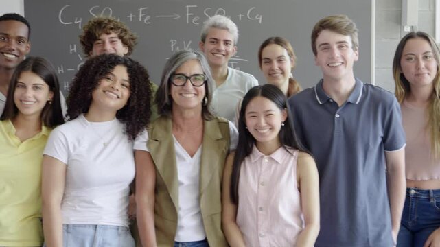 Portrait of a group of diverse teenage students and a female teacher smiling looking at camera in a class. High school, school year, university