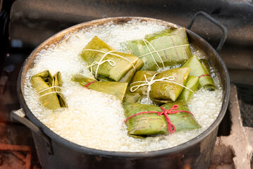 Tamales wrapped in banana leaves, tied with string, cooking in a large pot filled with boiling water outdoors. 
