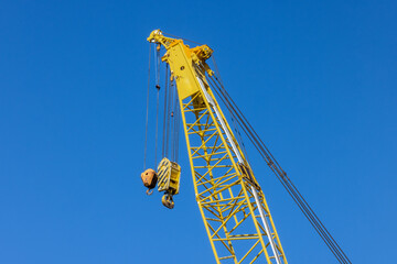 The top end of a yellow crane boom with two lifting hooks
