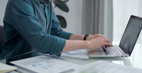 Entrepreneur wearing green shirt is working at laptop with data analysis charts. Businessman analyzing statistical data. Business concept