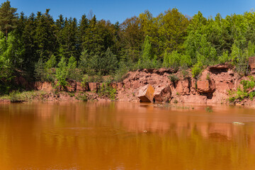 Landscape of an abandoned red sandstone quarry with water filling its bottom