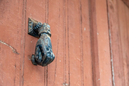 Old metal door handle in the shape of a hand on a wooden doo