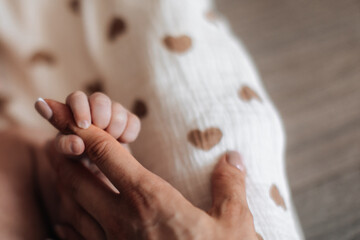 Tiny hand of newborn baby holding mother's finger, love family and motherhood concept
