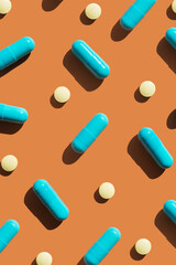 Pattern of blue and yellow pills on orange background. Creative tablets concept