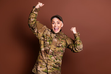 Photo portrait of attractive mature woman army soldier raise fists winning wear military uniform isolated on brown color background