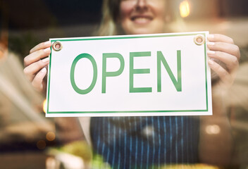 Hands, woman and glass door with open sign at cafe with smile for small business and customer service. Closeup, coffee shop and happy as waitress with poster card for operating time and hours