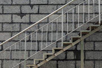 Metal staircase with a support with a metal railing on the background of a stone wall. The stones...