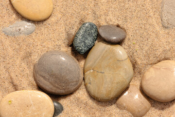 Stones of different sizes and designs are partially buried n the beach sand in late August at...