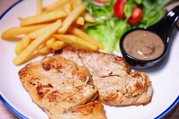 Chicken steak with side dishes of French fries, salad and pepper sauce on a white plate, photographed with studio lights.