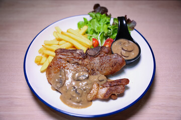 Pork chop steak with side dishes of French fries, salad and pepper sauce on a white plate, photographed with studio lights.