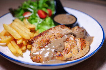Chicken steak with side dishes of French fries, salad and pepper sauce on a white plate, photographed with studio lights.
