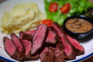 Medium rare steak, cut into bite-sized pieces, served with pepper sauce, mashed potatoes and salad.