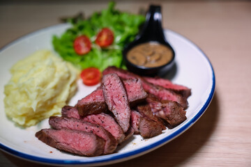 Medium rare steak, cut into bite-sized pieces, served with pepper sauce, mashed potatoes and salad.