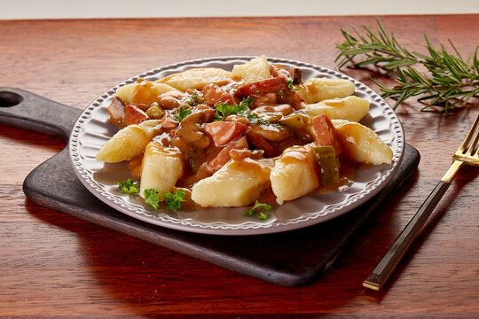 A hearty plate of Polish kopytka (potato dumplings) served with sausage stew and rich gravy, garnished with fresh parsley. A rustic, comforting dish perfect for a cozy and satisfying meal.