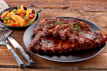 A plate of tender, juicy grilled pork ribs glazed with rich barbecue sauce, garnished with fresh thyme, is paired with a colorful side of roasted vegetables, including green beans, red peppers, sweet 