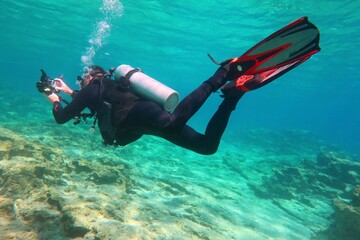 Shallow rocky seascape, clear ocean and swimming underwater photographer scuba diver. Travel picture, adventure trip. Scuba diver  underwater, seascape with blue green sea.