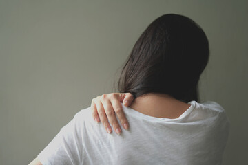 Tired young asian woman suffering neck pain while working for so long at home, exhausted young female rubbing and massaging her painful area and frowning, suffering osteoporosis or arthritis.