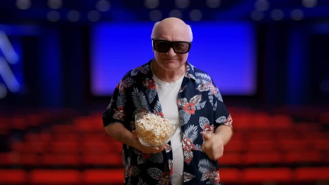 Funny grandpa wearing 3D glasses, eating popcorn and winking in cinema hall