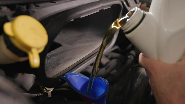 Pouring five quarts of dark synthetic motor oil into gasoline car engine for a sprinter van front out of a white bottle can in slow motion and close-up shot
