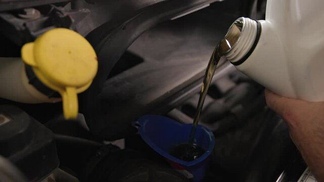 Pouring five quarts of dark synthetic motor oil into gasoline car engine for a sprinter van front out of a white bottle can in slow motion and close-up shot