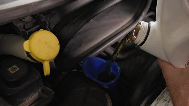 Pouring five quarts of dark synthetic motor oil into gasoline car engine for a sprinter van front out of a white bottle can in slow motion and close-up shot