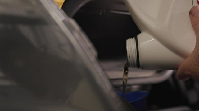 Pouring five quarts of dark synthetic motor oil into gasoline car engine for a sprinter van front out of a white bottle can in slow motion and close-up shot