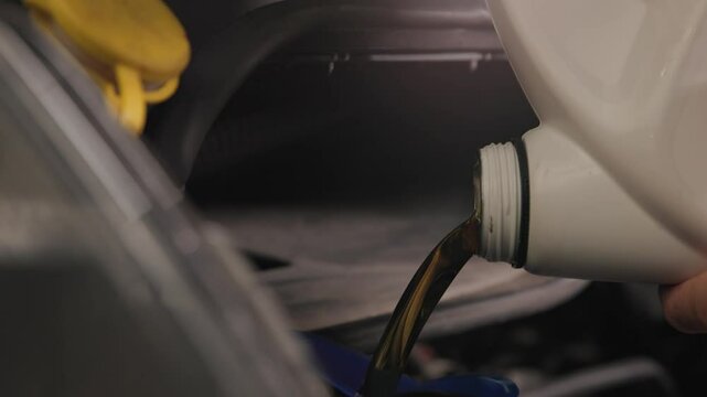 Pouring five quarts of dark synthetic motor oil into gasoline car engine for a sprinter van front out of a white bottle can in slow motion and close-up shot