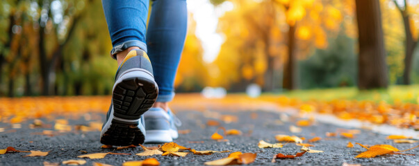 Close-up of person walking on a leaf-covered path in a park during autumn, focusing on legs and shoes.