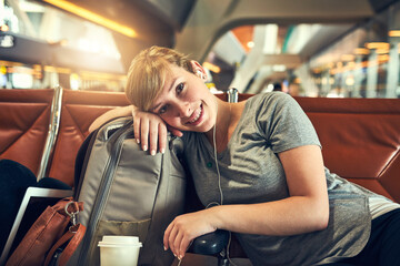 Happy woman, portrait and relax with earphones at airport in waiting room for flight, departure or travel. Young, female person or tourist with smile or headphones for trip or delay in Netherlands