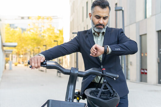 Businessman checking time while using electric bike in city