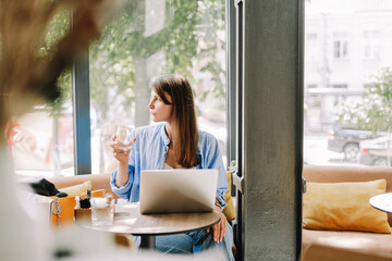 Young, attractive woman drinking water looking through window in cafe