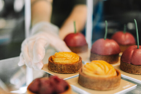 Pastry chef arranging delicious desserts on display in bakery selective focus