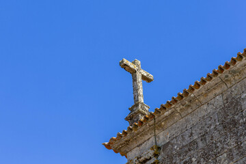 Religious christianity cross of granite on the roof of a church with a blue sky in Quintela...