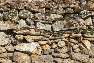 Detail of a granite wall with moss, large and small gray stones stacked on top of each other part of an old historic Portuguese house.