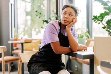 Tired waitress leaning on a table in a coffee shop looking away pensively