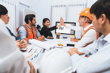 Diverse group of civil engineer and client celebrate and high five after make successful agreement on architectural project, reviewing construction plan and building blueprint at meeting table.Prudent