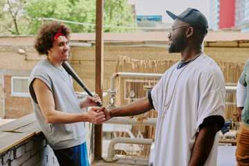 Curly haired man leaning on bricks while greeting his buddy in backyard