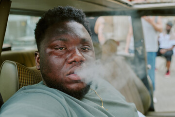 Rough man sitting in car and smoking, he looking directly at camera
