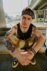 Young brutal rough man sitting on stairs and looking at camera
