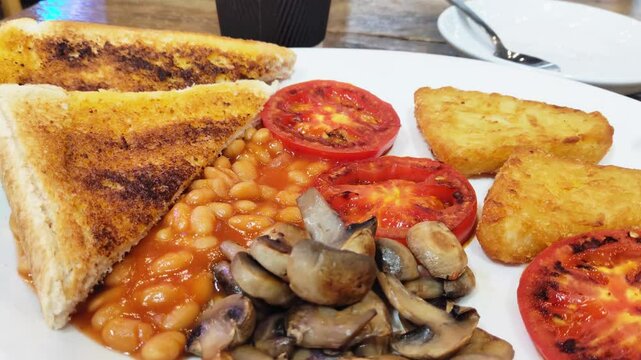 A plate of vegetarian breakfast with baked beans, toast, hash brown, grilled tomato, mushroom, and avo