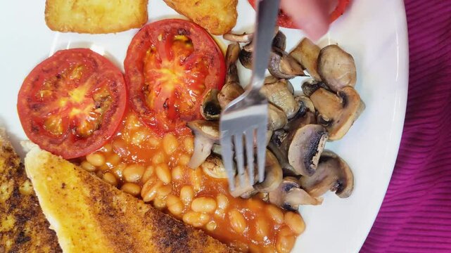 A plate of vegetarian breakfast with baked beans, toast, hash brown, grilled tomato, mushroom, and avo