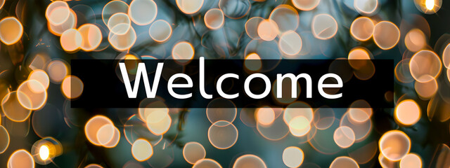 The text “Welcome” against a blurry background of lights. Welcome concept, signage at the entrance.