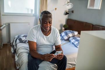 Senior black man using smartphone on bed at home