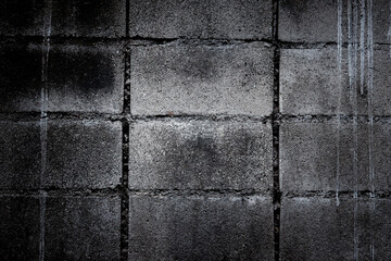 Fototapeta premium A wall made of gray bricks with a black background. The wall is covered in graffiti and has a rough texture